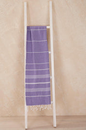 A model wearing the Hammamas Original Cotton Towel in colour Iris (Purple), from the front, showing the whole outfit
