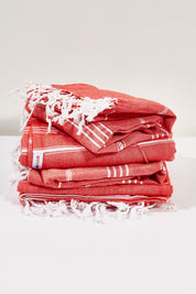 A model wearing the Hammamas Original Cotton Towel in colour Flame (Red), from the front, showing the whole outfit