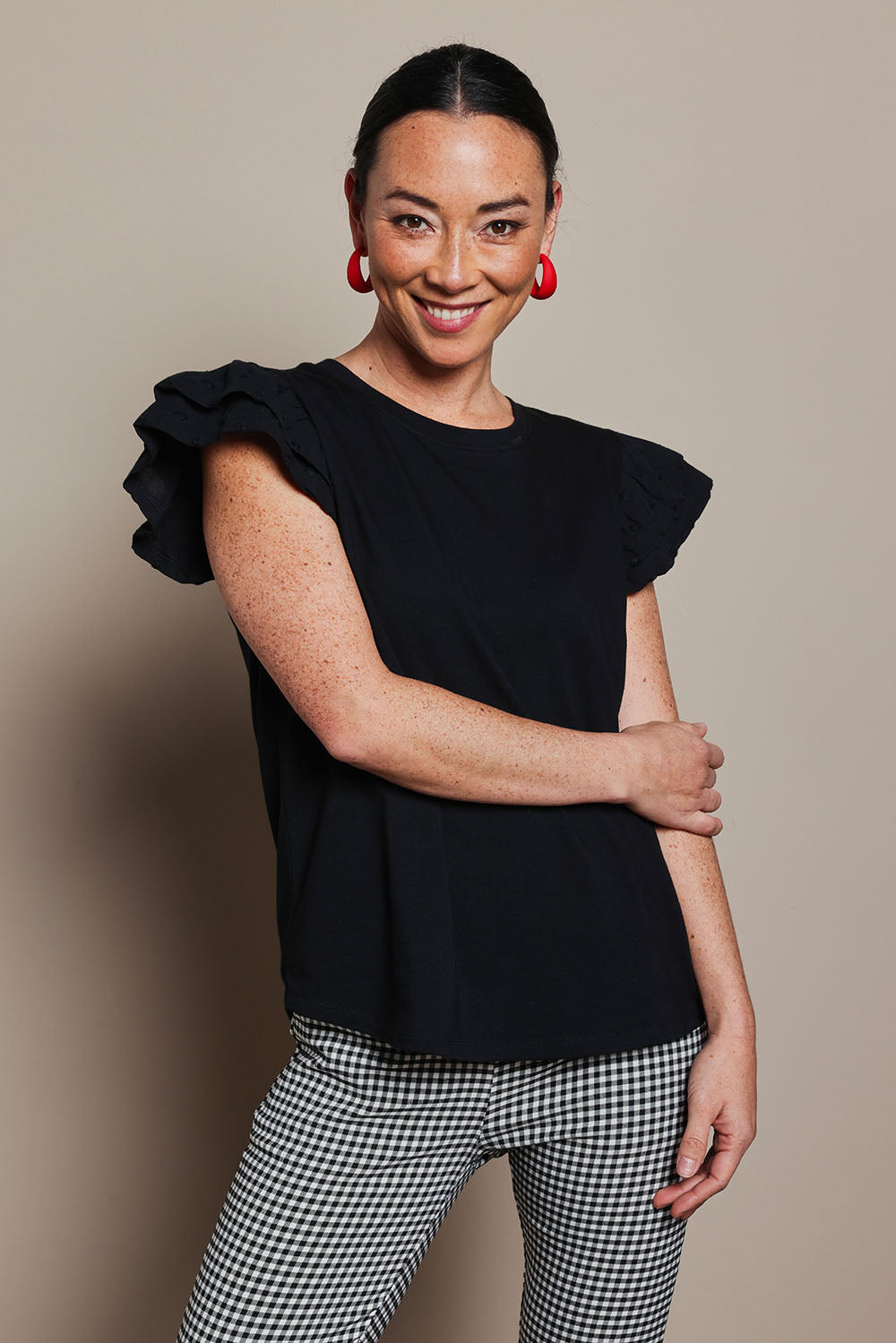 Model Katie wearing size 10 of the Ruffle Sleeve Top in colour Black (Black), from the front, cropped image