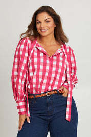 Model Monique wearing size 14 of the Printed Tie Neck Blouse in colour Berrycheck (Pink), from the front, cropped image