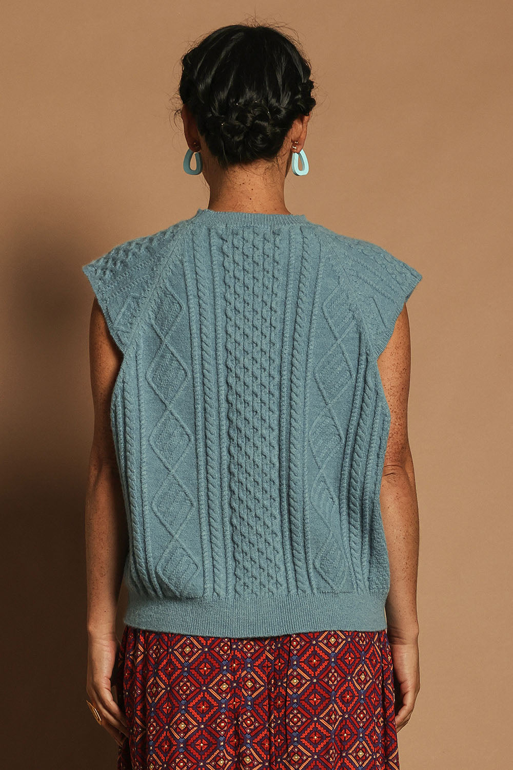 Model Katie wearing the Cable Vest in colour Bluehaze (Blue), from the back