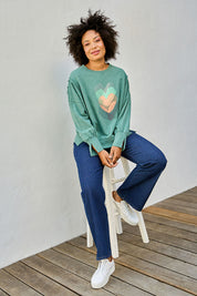Model Olivia wearing size 10 of the Heart Cotton Sweater in colour Hearts (Green), from the front, showing the whole outfit