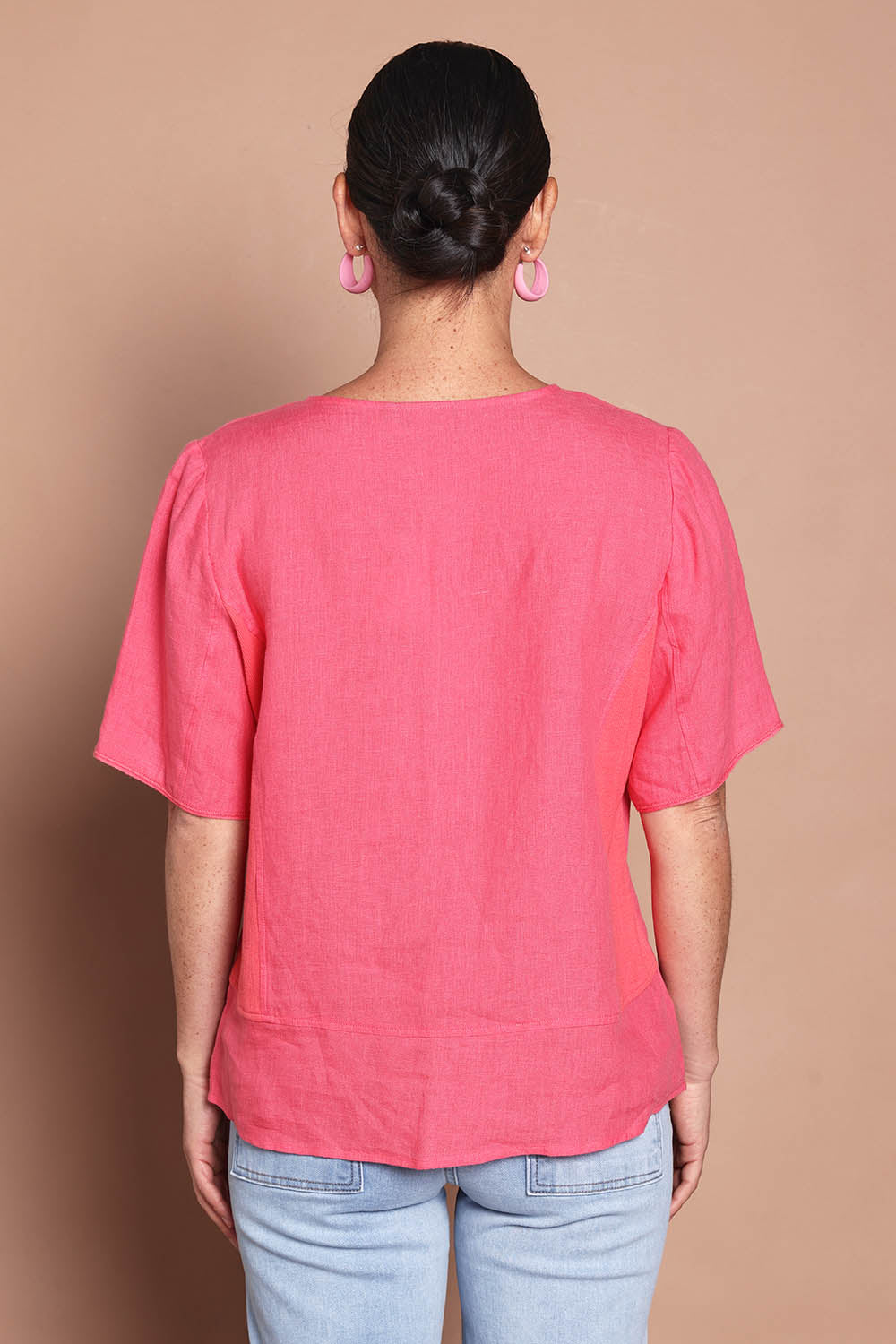 Model Katie wearing size 10 of the Linen Elastane V Neck Blouse in colour Melon (Pink), from the back