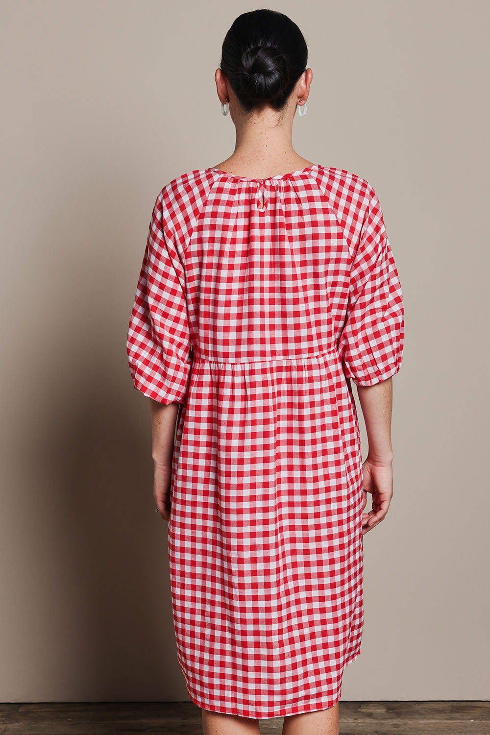 Model Katie wearing size 10 of the Cotton Empire Waist Dress in colour Ginghamred (Red), from the back