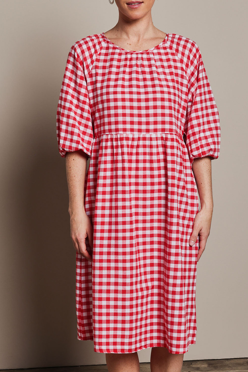 Model Katie wearing size 10 of the Cotton Empire Waist Dress in colour Ginghamred (Red), from the front, cropped image