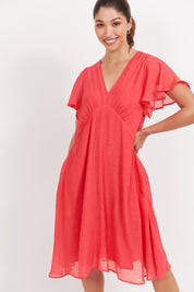A model wearing the Baja Dress in colour Punch (Red), from the front, cropped image