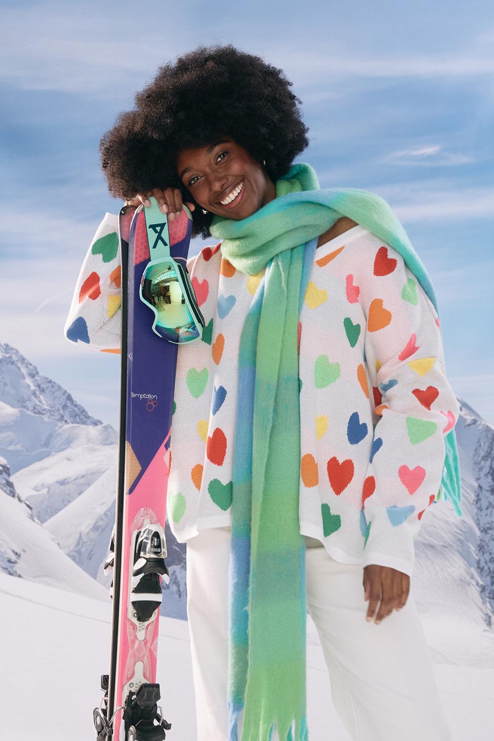 A model wearing the Alaska Relaxed Heart Jumper in colour Rainbow, from the front, showing the whole outfit