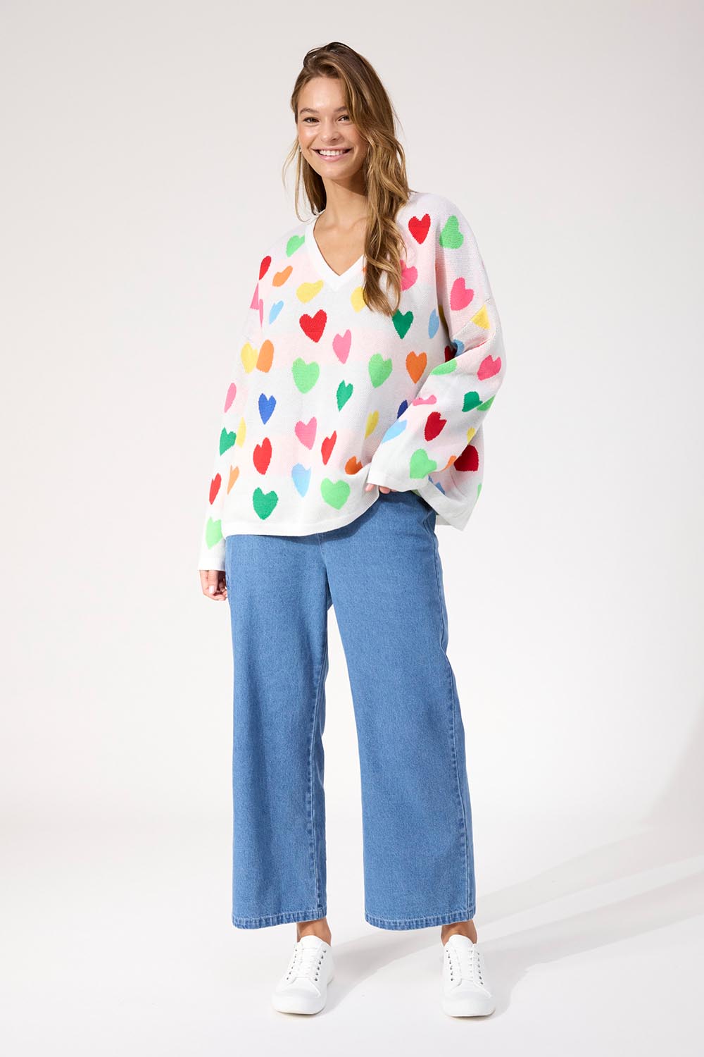 A model wearing the Alaska Relaxed Heart Jumper in colour Rainbow, from the front, showing the whole outfit
