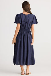A model wearing the Blossom Linen Dress in colour Navy (Blue), from the back