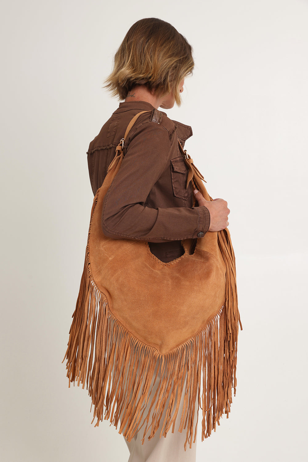 A model wearing the Folklore Suede Bag in colour Tan, from the front, cropped image