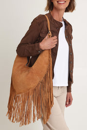 A model wearing the Folklore Suede Bag in colour Tan, from the front, cropped image