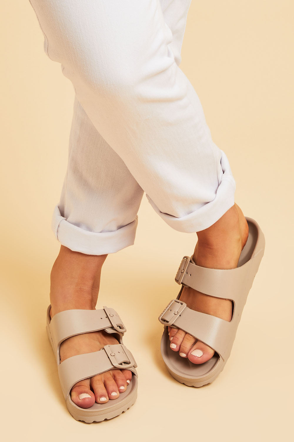 A model wearing size 7 of the Sundreamer EVA Slide in colour Sand, from the front, cropped image