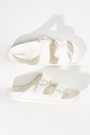 A model wearing size 6 of the Sundreamer EVA Slide in colour White (White), from the front, showing the whole outfit