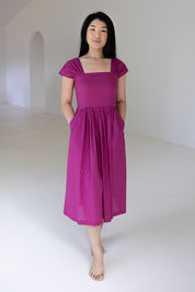 A model wearing the Leanne Dress in colour Violet (Purple), from the front, showing the whole outfit