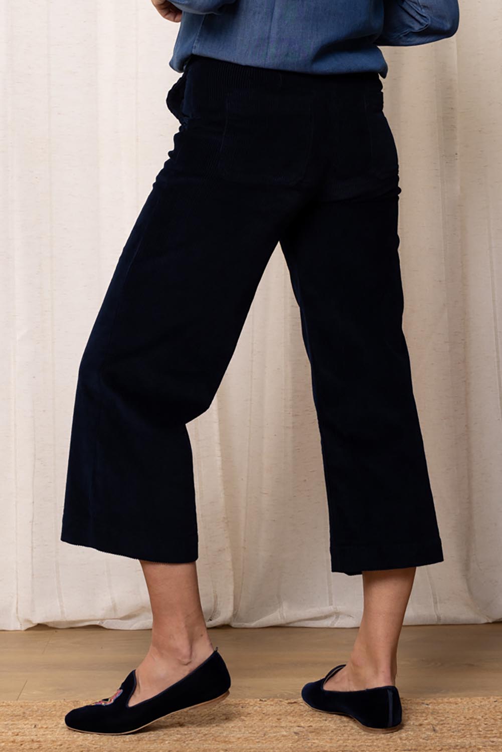 A model wearing the Isla Crop Cotton Cord Trouser in colour Navy (Blue), from the back