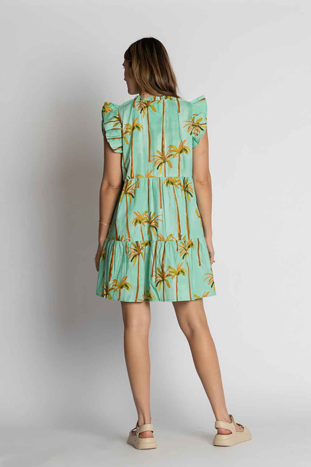 A model wearing the Badira Cotton Ruffle Dress in colour Mist (Green), from the back