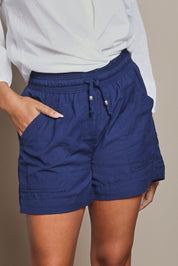 Model Ziara wearing size S of the Cotton Beach Short in colour Navy (Blue), from the front, cropped image