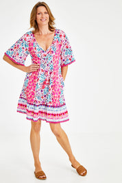 Model Naomi wearing size S of the Jordan Shirred Dress in colour Melon (Pink), from the front, showing the whole outfit