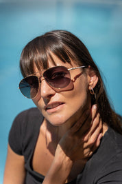 A model wearing the Mara Sunglasses in colour Gold (Metallics), from the front, showing the whole outfit
