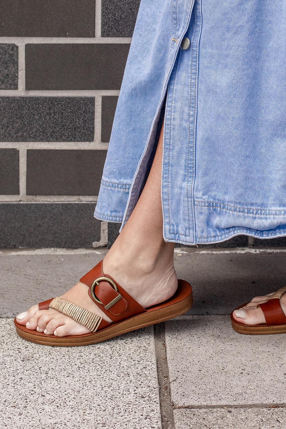 A model wearing the Bria Flat Sandal in colour Cognac, from the front, cropped image