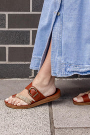A model wearing the Bria Flat Sandal in colour Cognac, from the front, cropped image