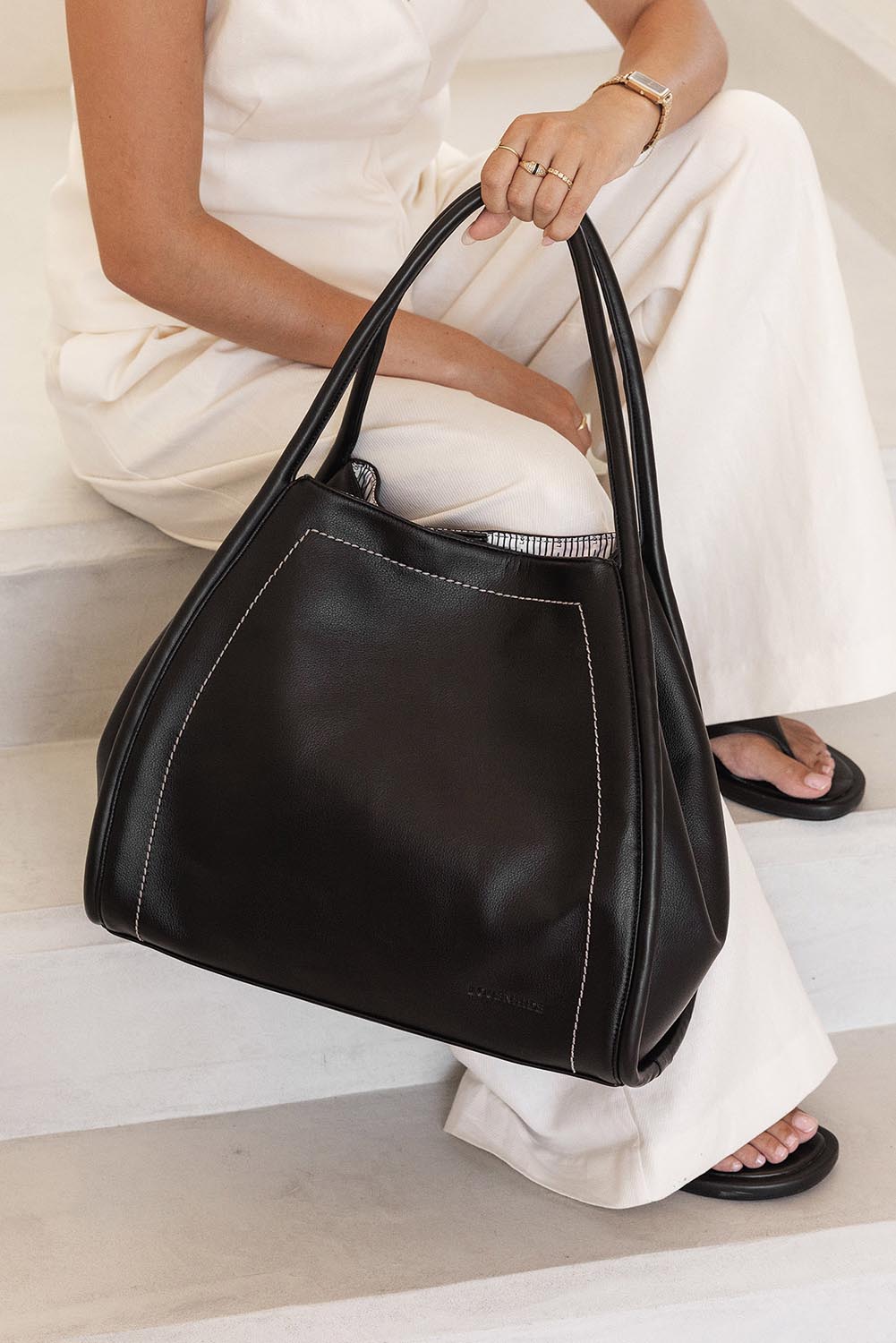 A model wearing the Sutton Shoulder Bag in colour Black (Black), from the front, showing the whole outfit
