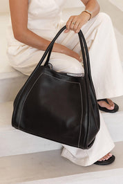 A model wearing the Sutton Shoulder Bag in colour Black (Black), from the front, showing the whole outfit