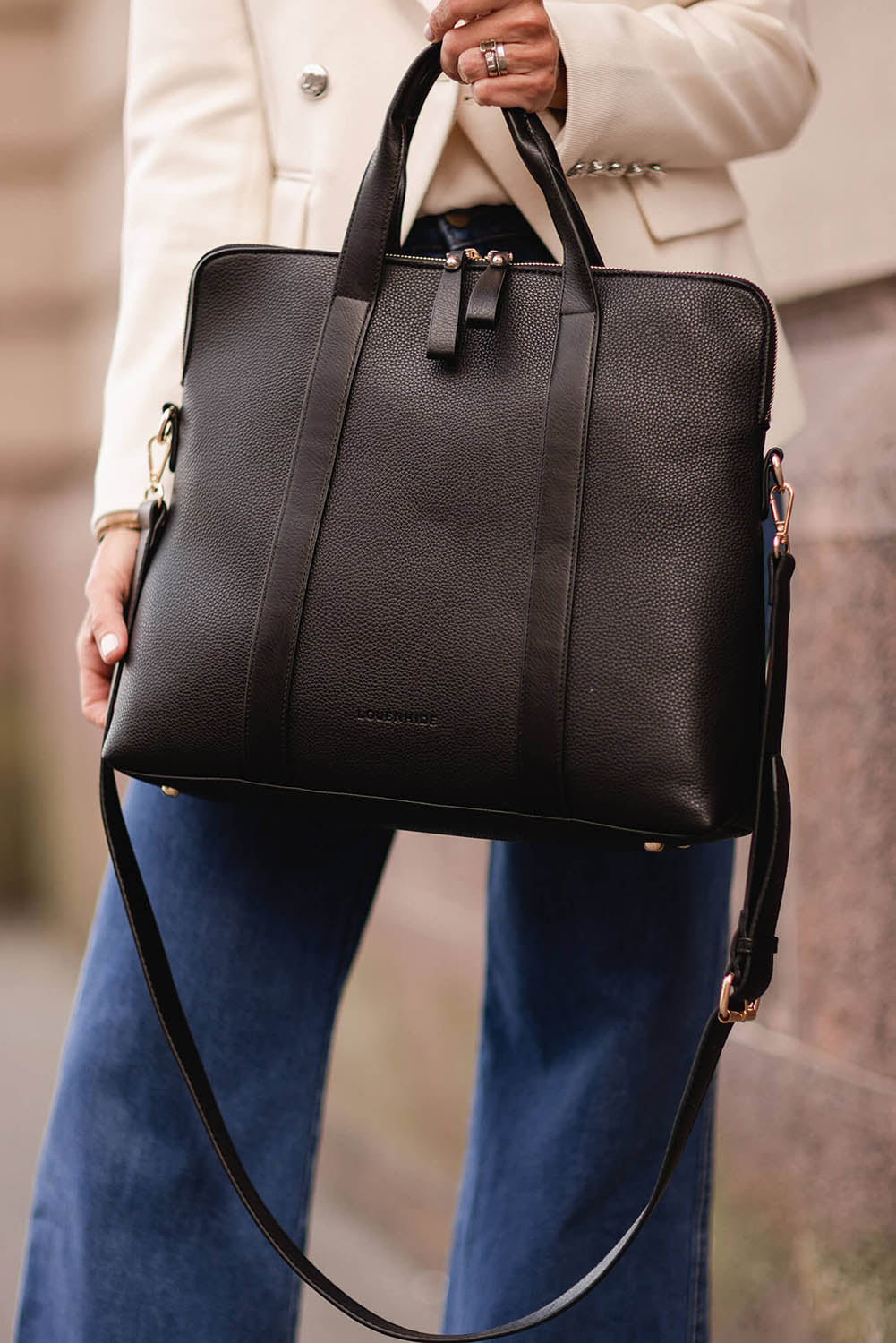 A model wearing the Rhodes Laptop Bag in colour Black (Black), from the front, showing the whole outfit
