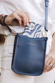 A model wearing the Parker Phone Crossbody Bag in colour Navy (Blue), from the front, showing the whole outfit