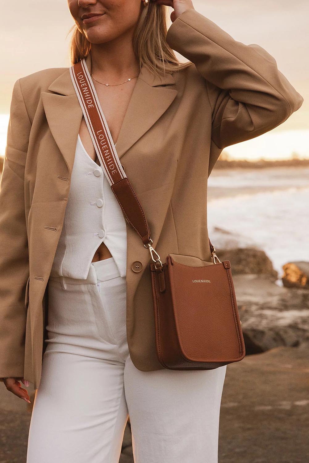 A model wearing the Parker Phone Crossbody Bag in colour Tanlogo, from the front, showing the whole outfit