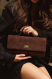 A model wearing the Delaney Suedette Clutch Handbag in colour Chocolate, from the front, showing the whole outfit