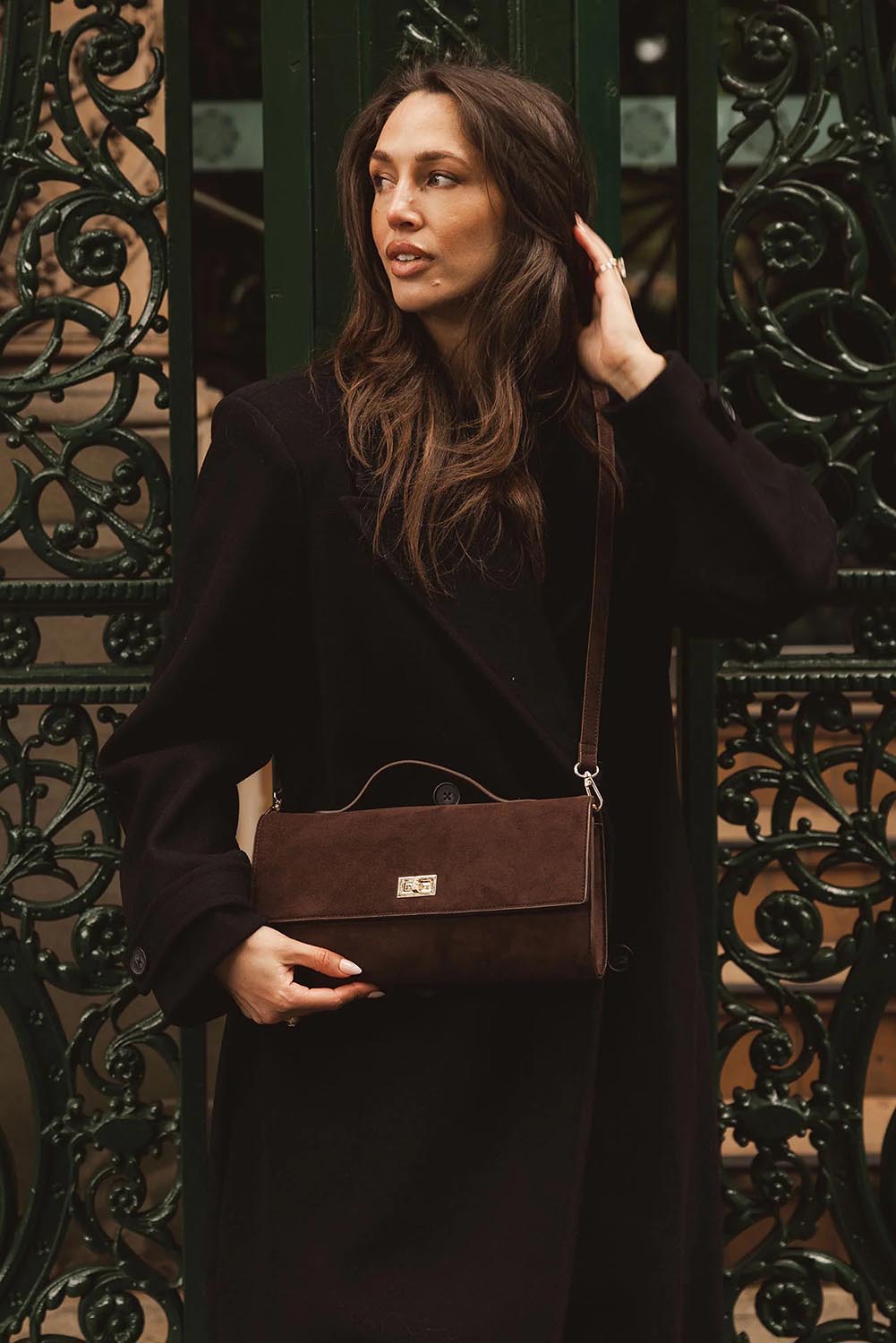 A model wearing the Delaney Suedette Clutch Handbag in colour Chocolate, from the front, showing the whole outfit