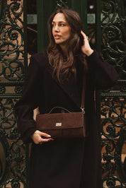 A model wearing the Delaney Suedette Clutch Handbag in colour Chocolate, from the front, showing the whole outfit