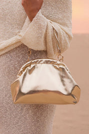 A model wearing the Lotus Clutch Bag in colour Gold (Metallics), from the front, showing the whole outfit