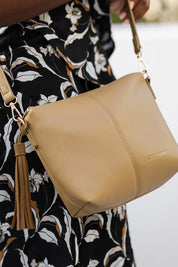 A model wearing the Kasey Crossbody Bag in colour Latte, from the front, cropped image