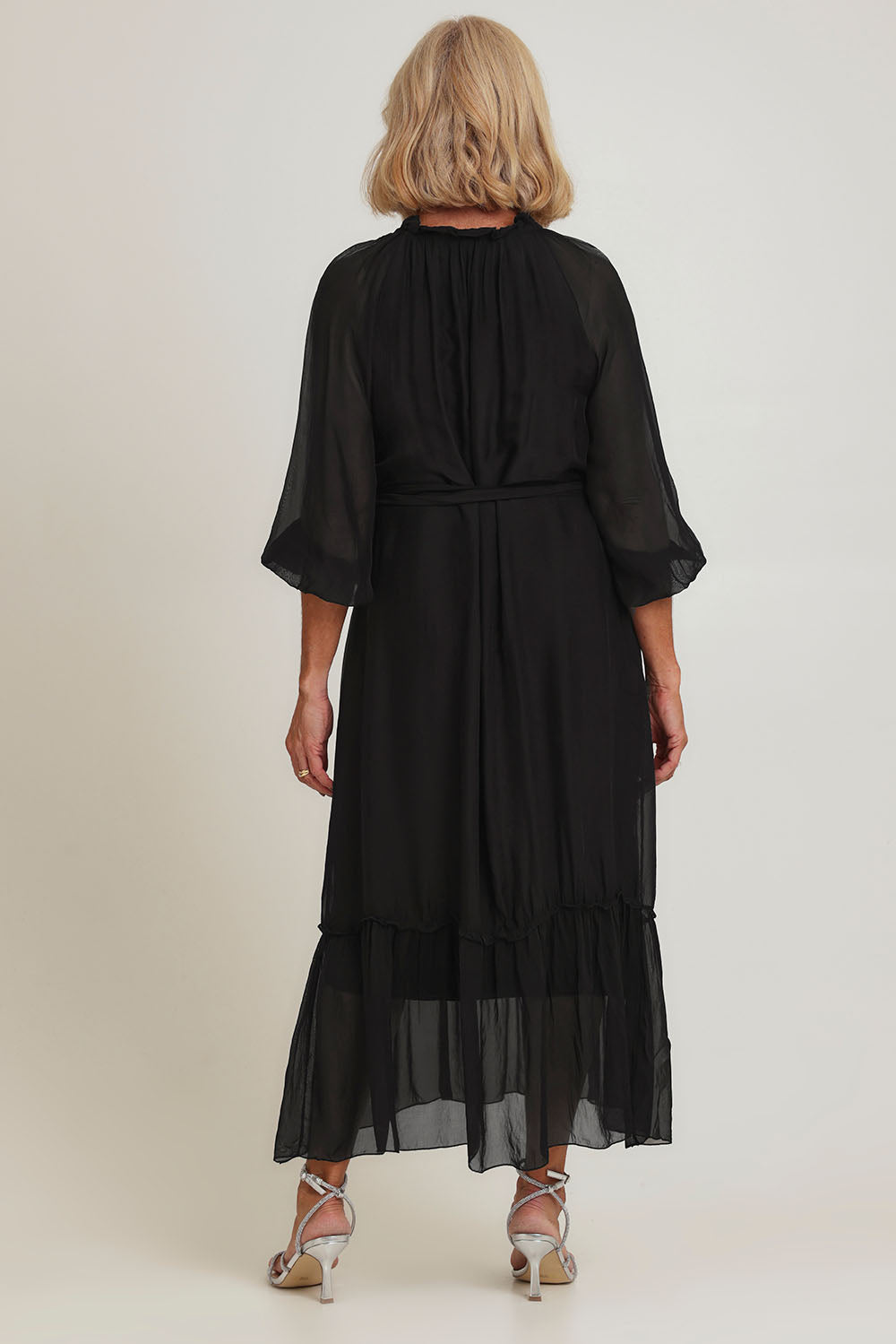 Model Sandy wearing the Long Sleeve Silk Frill Tied Neck Dress in colour Black (Black), from the back