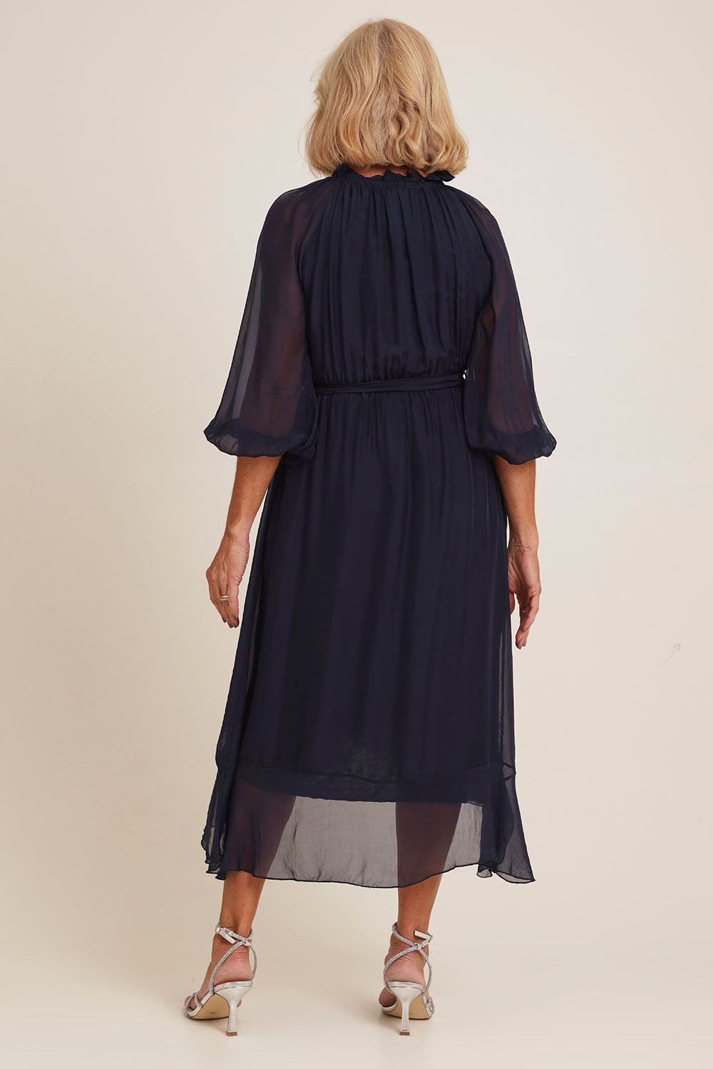Model Sandy wearing the Long Sleeve Silk Frill Tied Neck Knee Length Dress in colour Navy (Blue), from the back