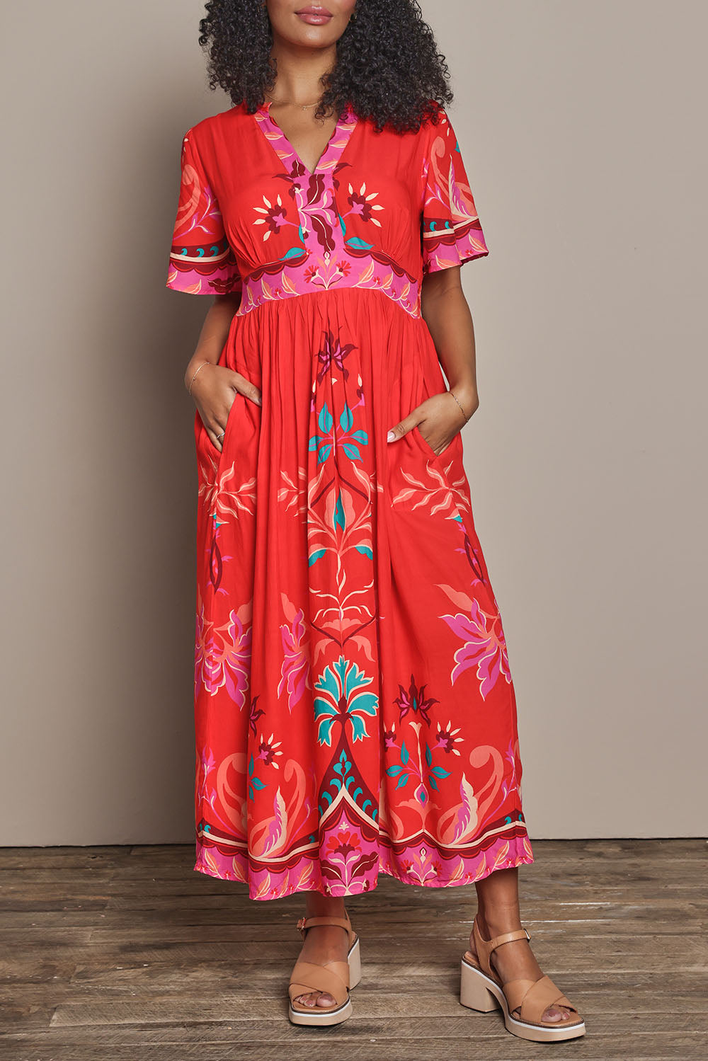 Model Ziara wearing size S of the Bahia Midi Dress in colour Geranium, from the front, cropped image