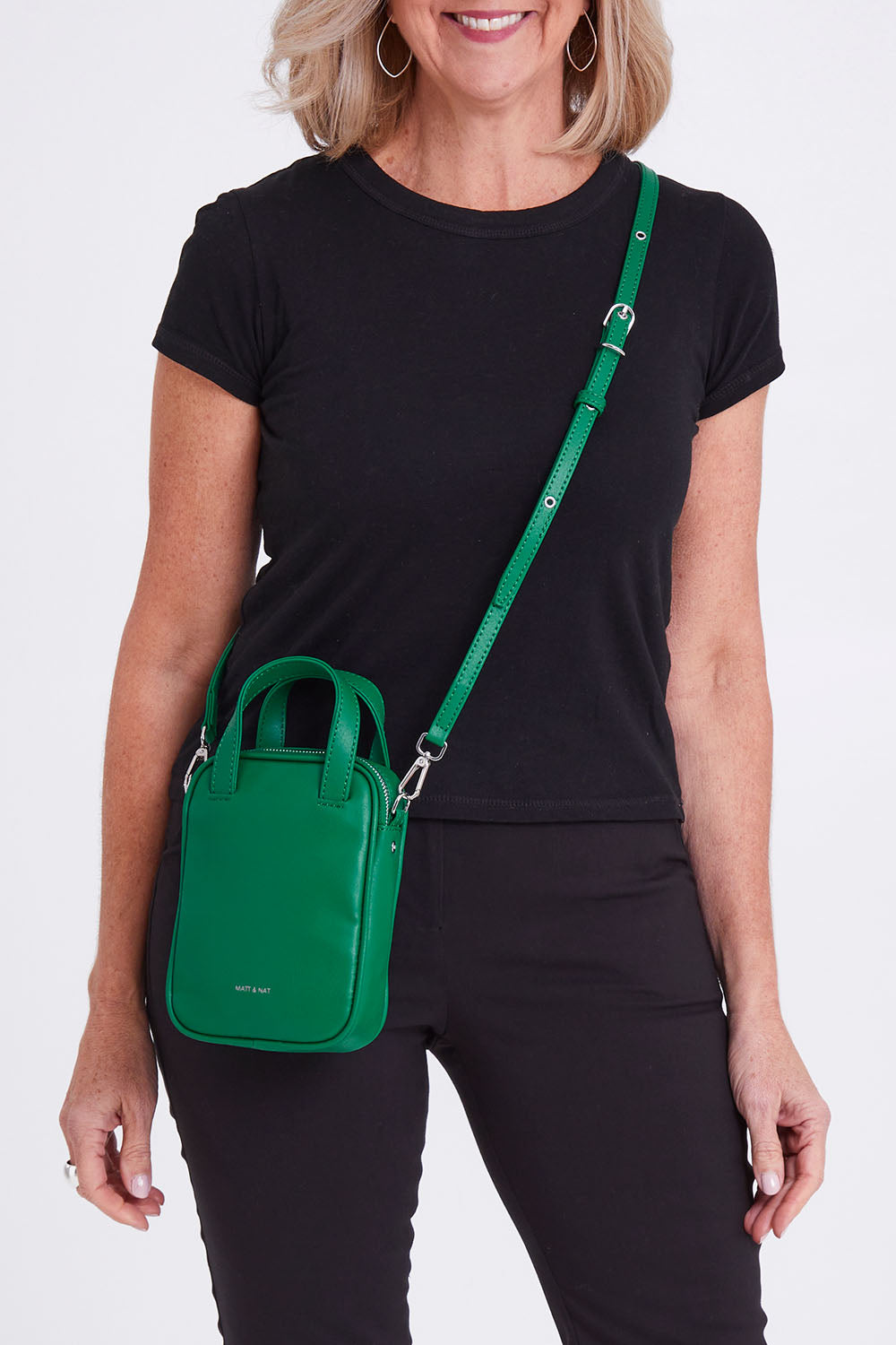 Model Sandy wearing size OneSize of the Leap Vegan Crossbody Bag in colour Peacock (Green), from the front, cropped image