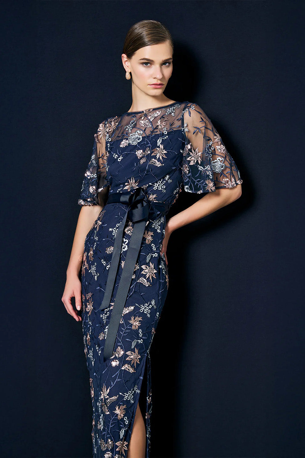 A model wearing the Florence Navy Embroidered Gown in colour Navy (Blue), from the front, showing the whole outfit