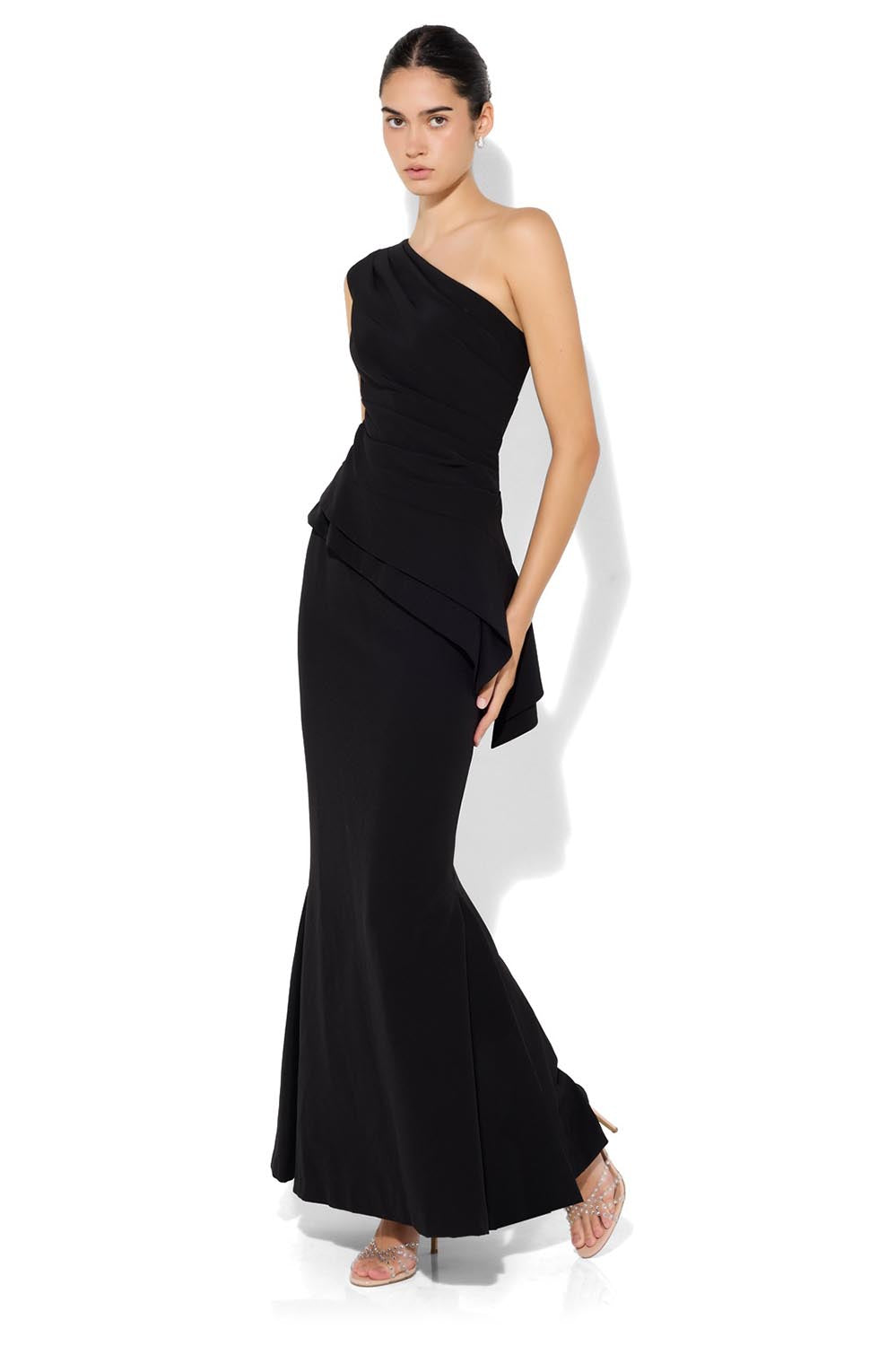 A model wearing the Oscar One Shoulder Gown in colour Black (Black), from the front, showing the whole outfit