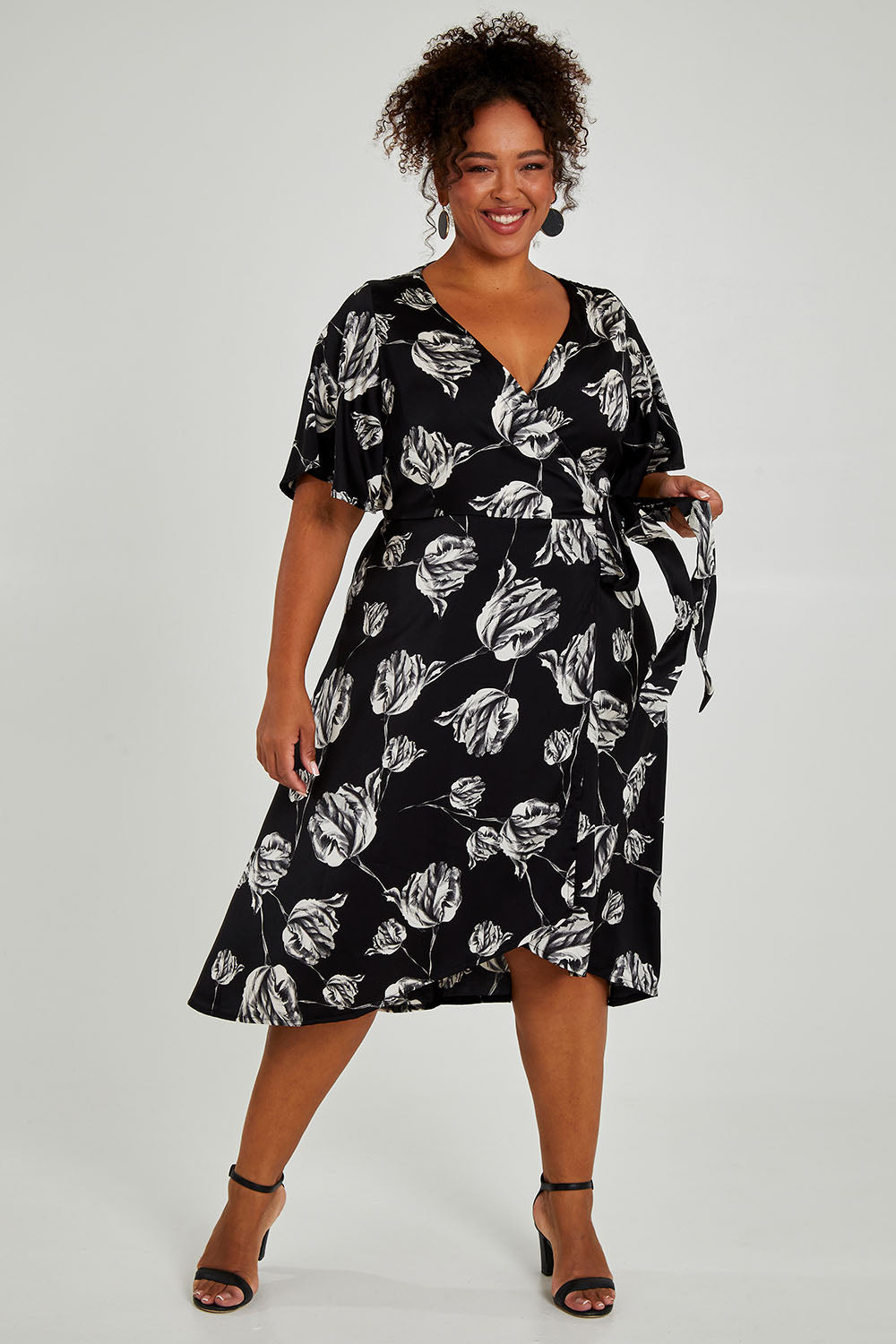 Model Alexis wearing size 16 of the Alanah Wrap Dress in colour Tulips (Black), from the front, showing the whole outfit