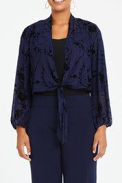Model Noli wearing size 14 of the Penny Shrug in colour Navyfleur (Blue), from the front, cropped image