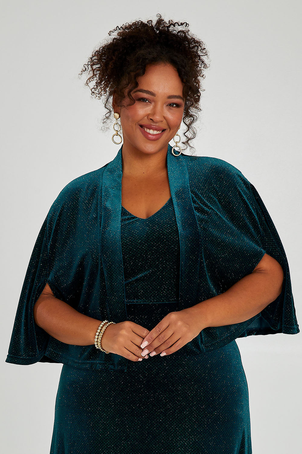 Model Alexis wearing size 16 of the Lynette Velvet Cape in colour Jade (Green), from the front, cropped image