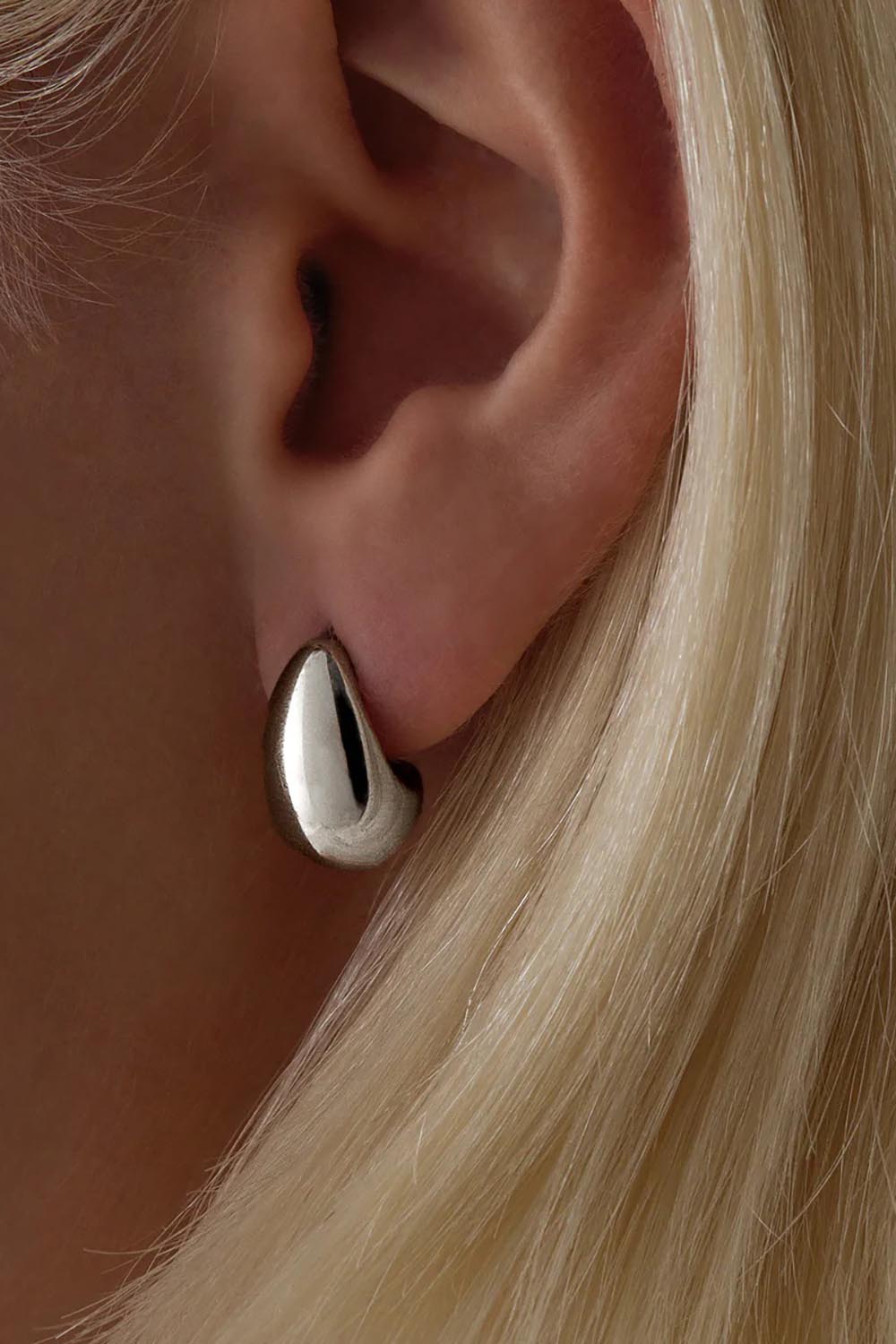 A model wearing the Baby Umbra Silver Earrings in colour Silver (Metallics), from the front, cropped image
