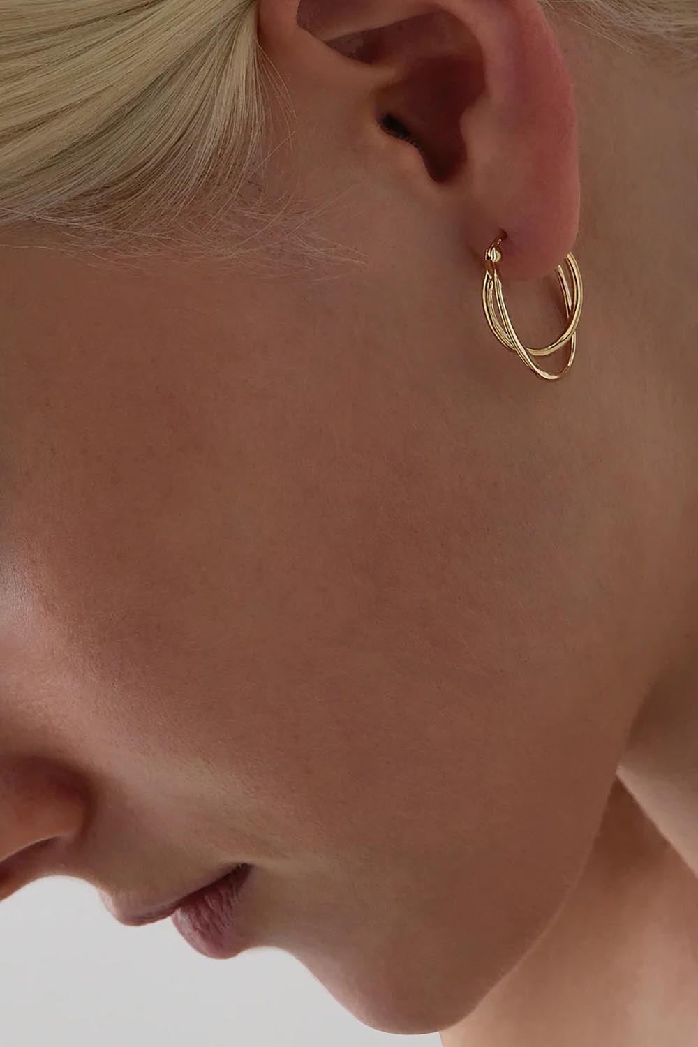 A model wearing the Eclipse Yellow Gold Hoop Earrings in colour Gold (Metallics), from the front, cropped image