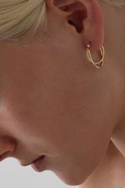 A model wearing the Eclipse Yellow Gold Hoop Earrings in colour Gold (Metallics), from the front, cropped image