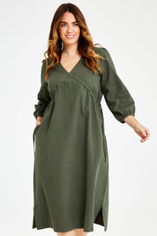 Model Laura wearing size 14 of the Ramie Empire Line Dress in colour Green (Green), from the front, cropped image