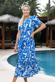 A model wearing the Cannes Ruched Waist Dress in colour Print (Blue), from the front, showing the whole outfit