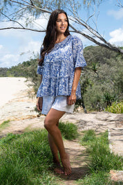 A model wearing the Cappadocia Organic Cotton Frill Sleeve Top in colour Blue (Blue), from the front, showing the whole outfit